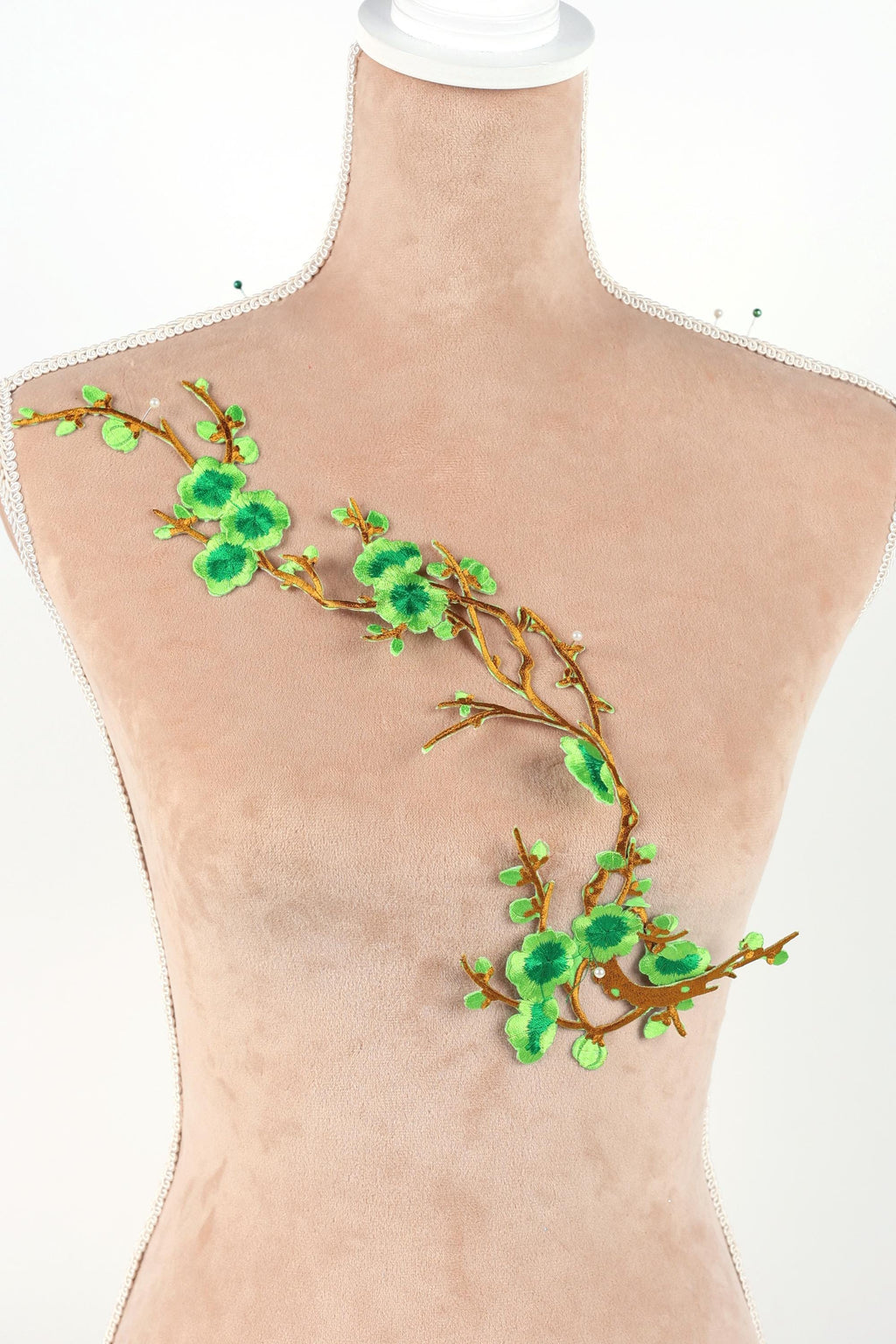 A mannequin torso with a decorative green leaf and branch embroidered on it.