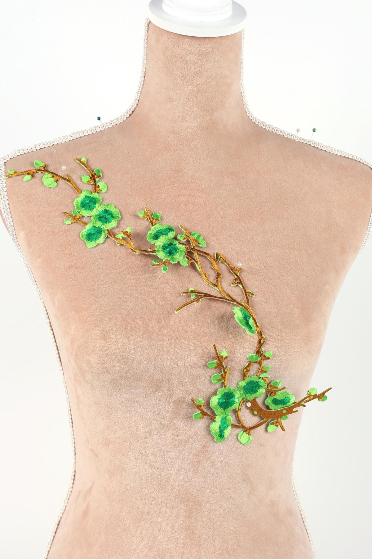 A mannequin torso with a decorative green leaf and branch embroidered on it.