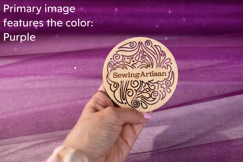 A hand holding a wooden coaster with the text "SewingArtisan" on it, against a purple background.