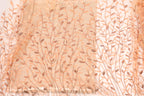 a close-up view of a fabric with a repeating pattern of leaves and branches in shades of peach and brown.