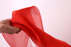 A hand is holding a red fabric, which appears to be a sheer or sheer-like material.