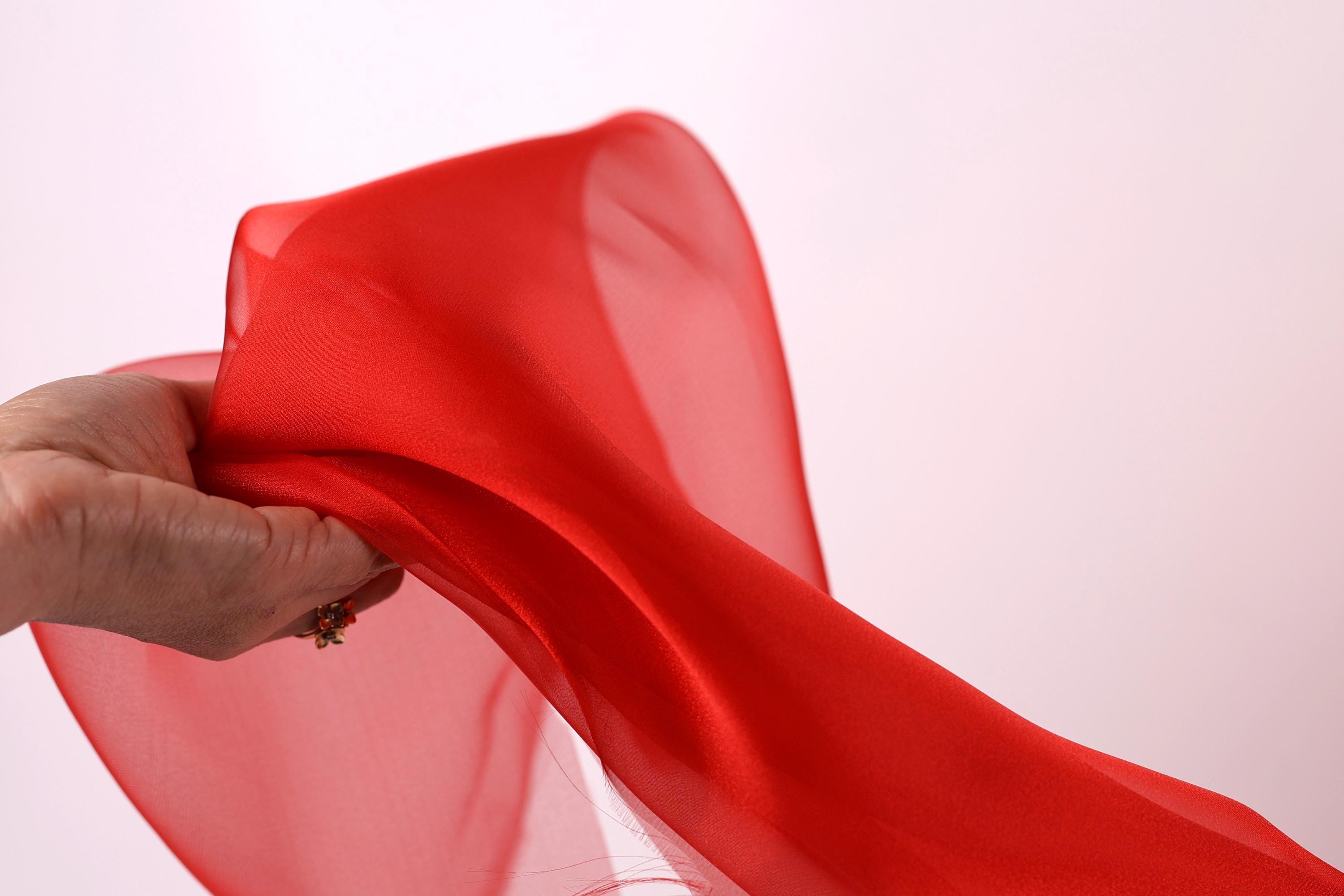 A hand is holding a red fabric, which appears to be a sheer or sheer-like material.