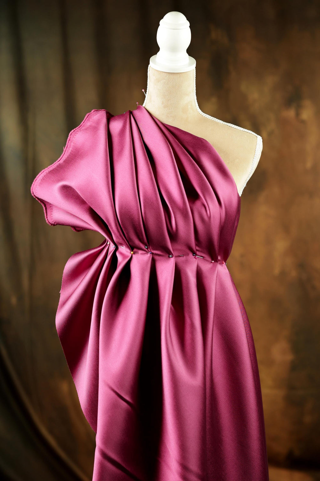 A mannequin wearing a vibrant, one-shoulder pink satin dress with a draped, flowing silhouette.