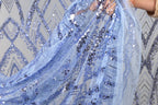 A close-up view of a hand holding a piece of blue sequin fabric, with the fabric's intricate patterns and textures visible.