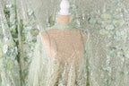 a mannequin wearing a sheer, green and white floral fabric draped over it. The fabric has a shimmering, sequined appearance, creating a visually striking and elegant effect.