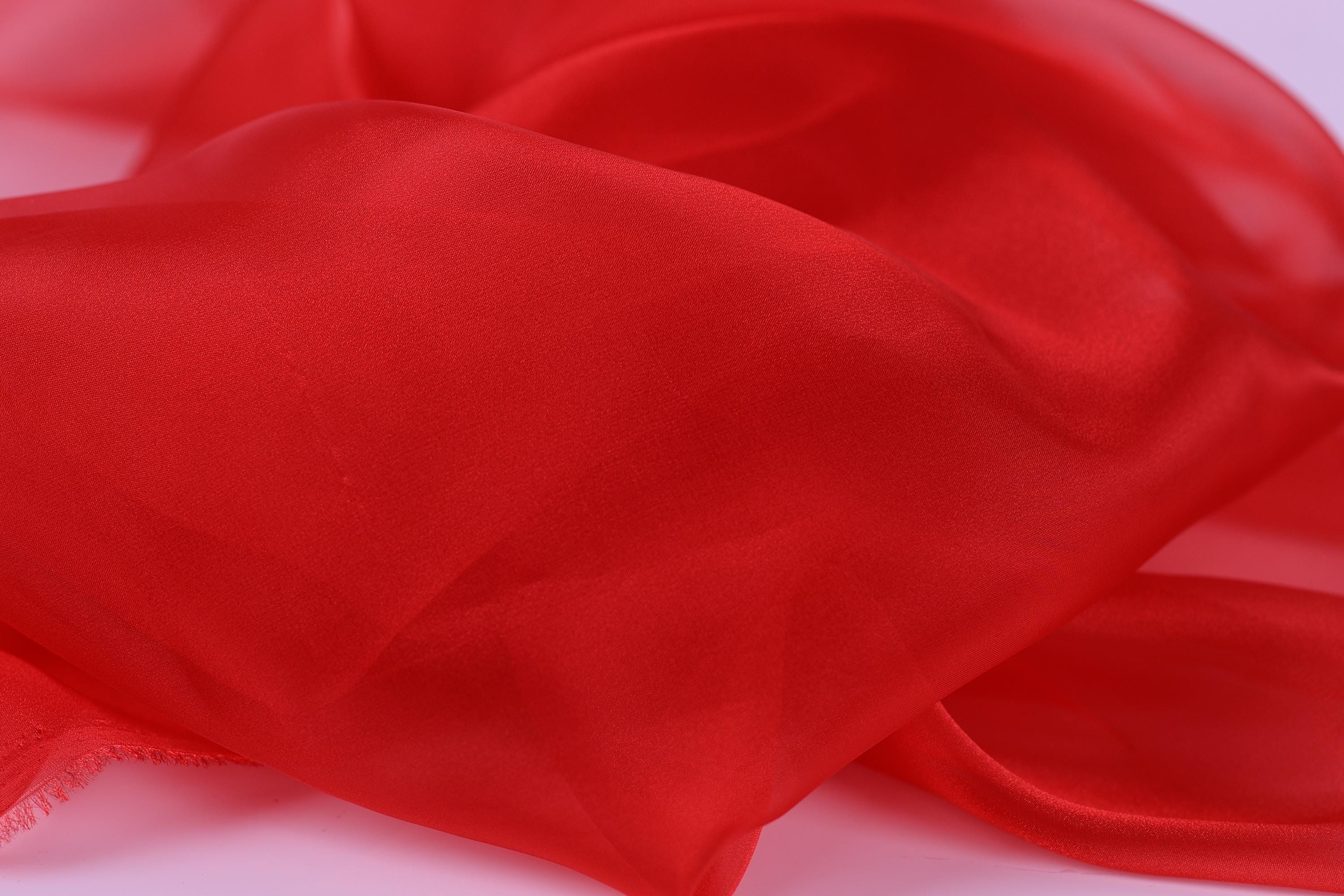 The image is a close-up of a red fabric, possibly silk or chiffon, with a soft, flowing texture.