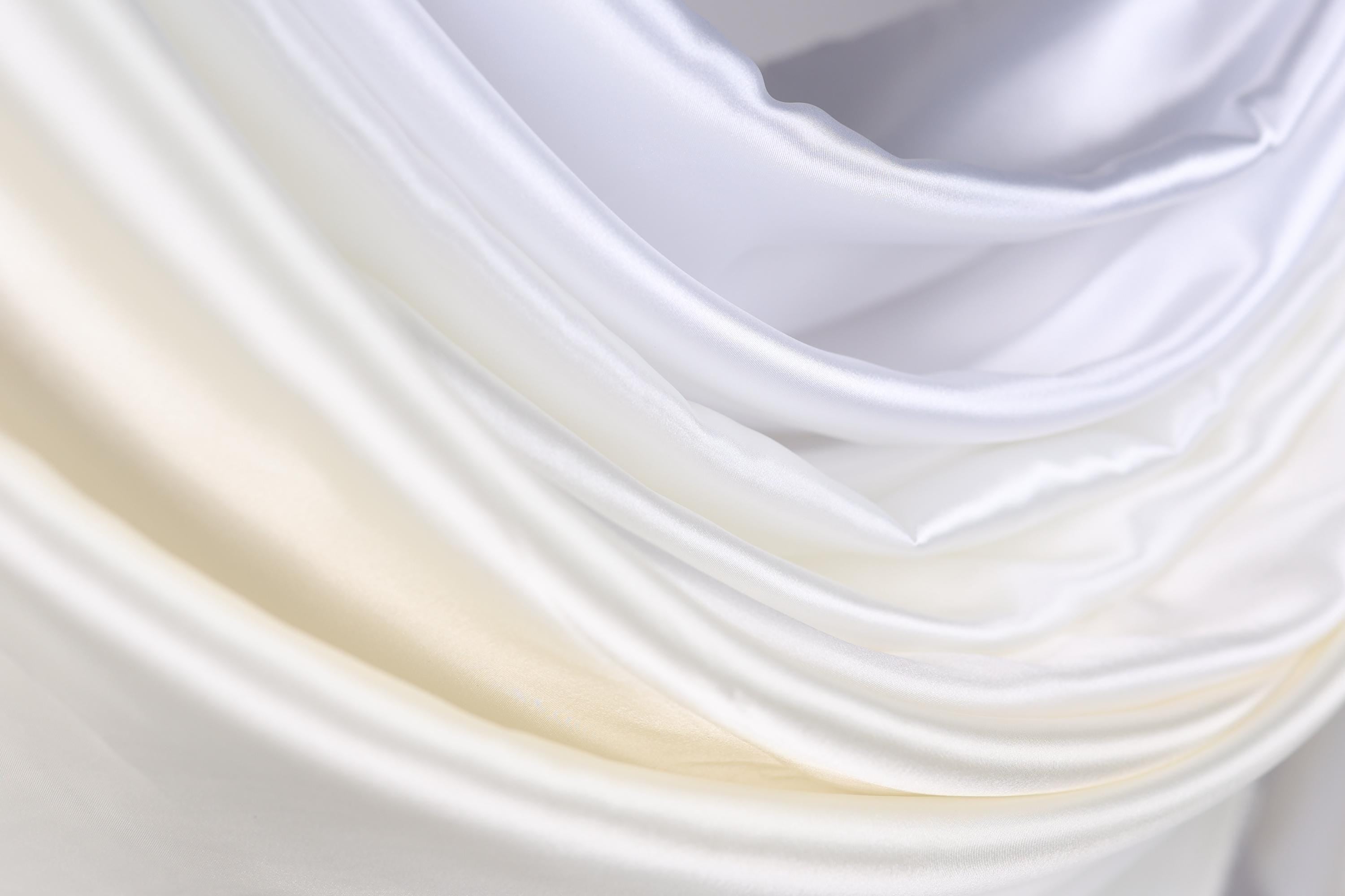 The image is a close-up of a soft, flowing fabric with a gradient of white and yellow colors. The fabric appears to be made of silk or satin, and it has a smooth, shiny texture. The colors are vibrant and create a visually appealing contrast.