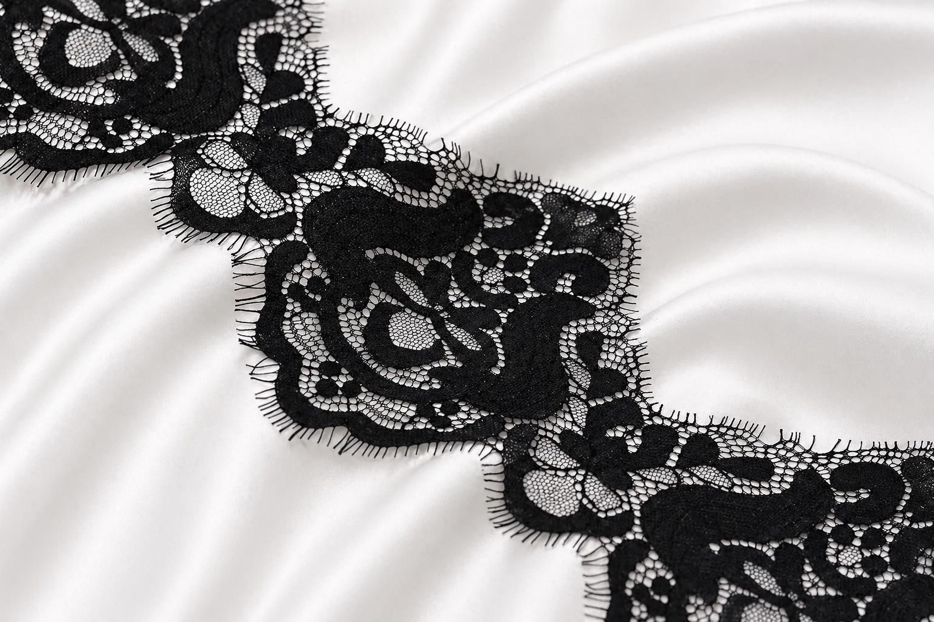 a close-up view of a delicate black lace pattern on a white fabric surface.