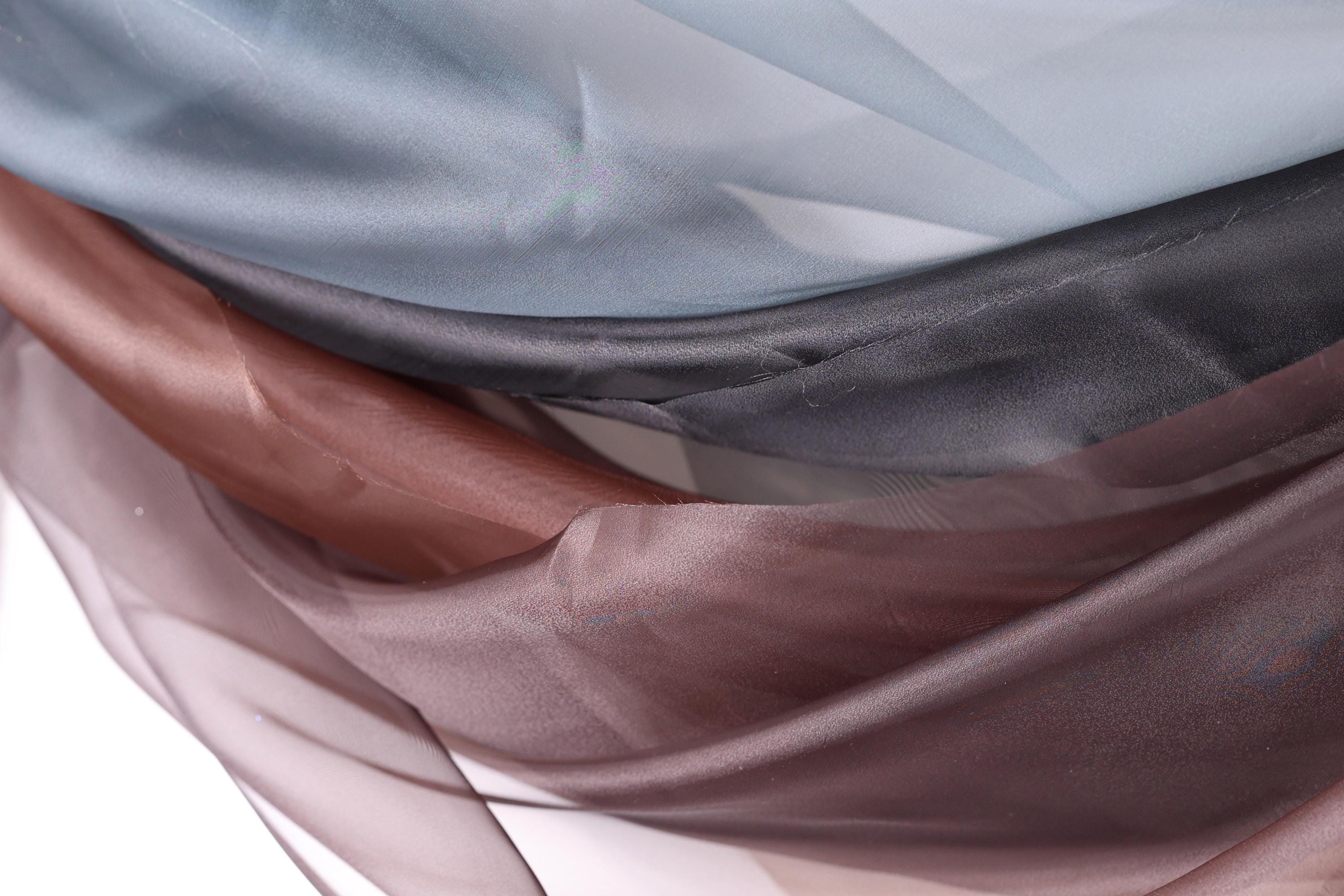a close-up view of a fabric with a mix of colors, including shades of blue, brown, and gray. The fabric appears to be made of silk or a similar material, and it has a textured and wrinkled appearance.