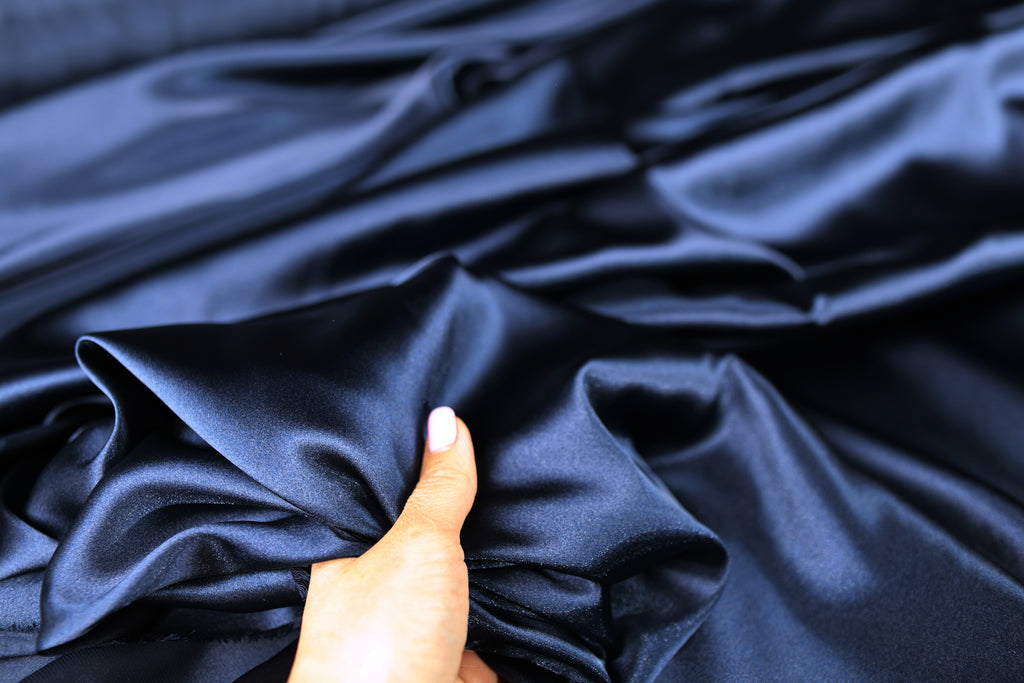 A hand is holding a piece of blue satin fabric, with the fabric's folds and creases visible.