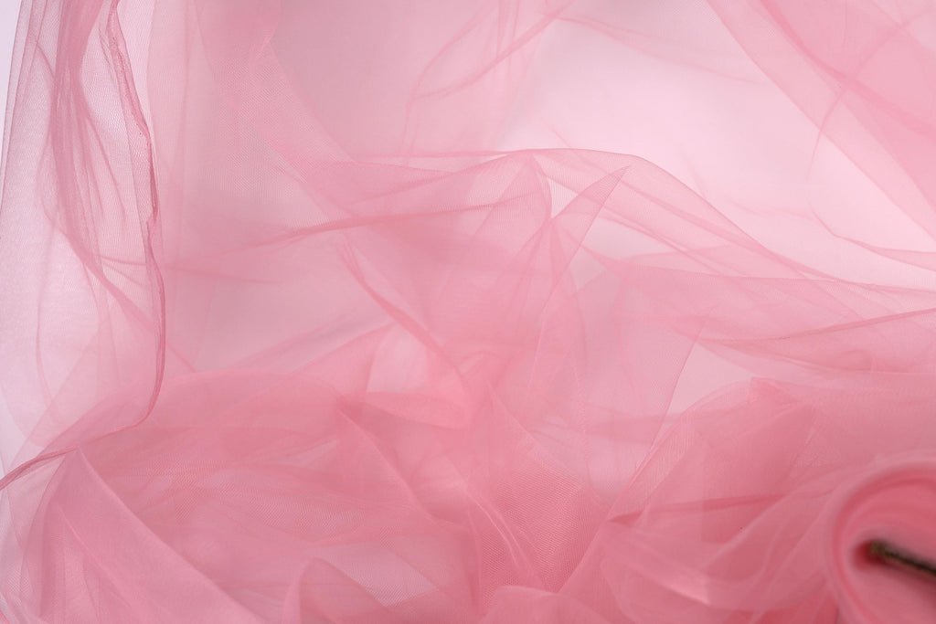 The image is a close-up of a soft, flowing pink fabric, possibly tulle, with a slightly wrinkled texture.
