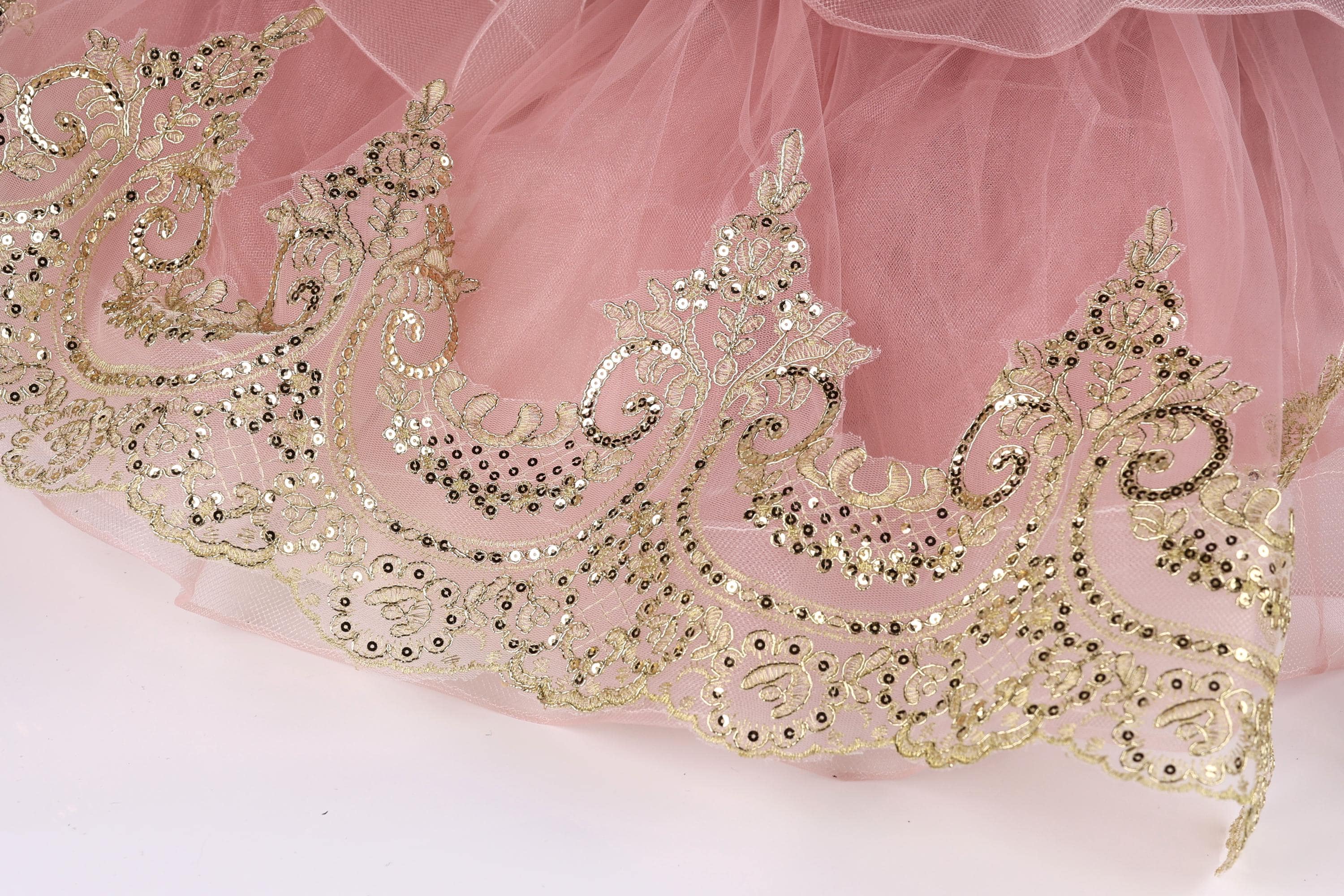a close-up view of a delicate, pink tulle skirt with intricate gold embroidery and sequins.