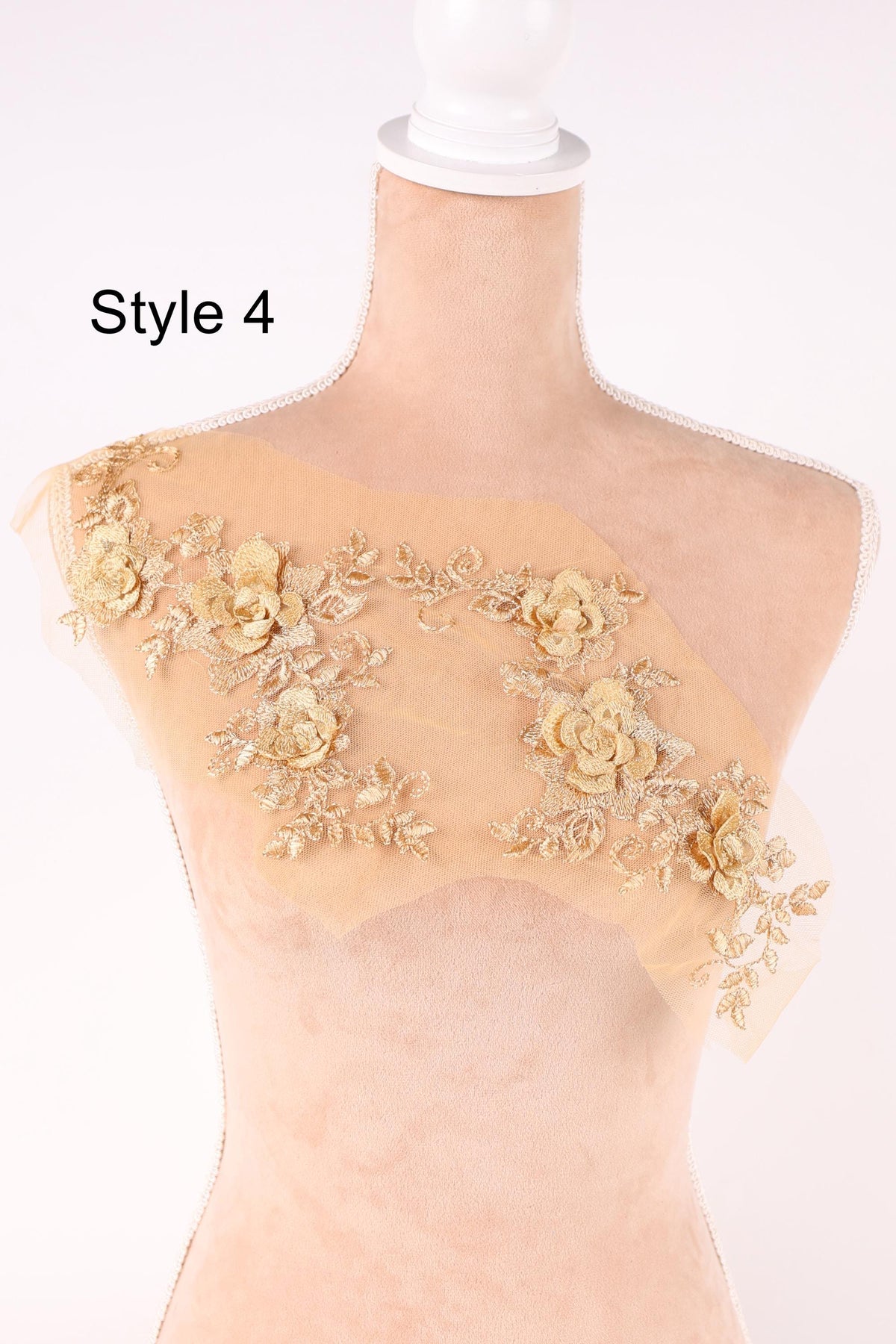 A mannequin wearing a beige dress with gold floral embroidery on the shoulder.