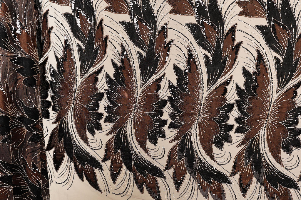 a close-up view of a fabric with a repeating pattern of brown and black flowers or leaves. The pattern is intricate and detailed, with the flowers and leaves appearing to be made of sequins or other embellishments. The fabric has a textured appearance, suggesting it could be a piece of clothing or textile.