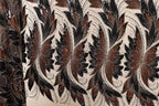 a close-up view of a fabric with a repeating pattern of brown and black flowers or leaves. The pattern is intricate and detailed, with the flowers and leaves appearing to be made of sequins or other embellishments. The fabric has a textured appearance, suggesting it could be a piece of clothing or textile.