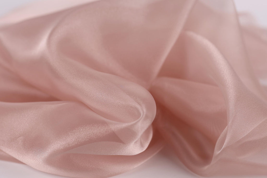 A close-up view of a soft, flowing pink fabric, possibly silk or chiffon, with a delicate and ethereal texture.