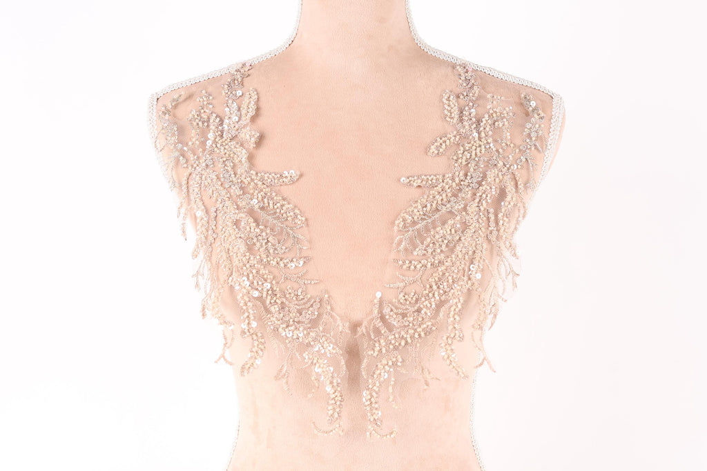 A mannequin wearing a beige dress with intricate lace and sequin details on the shoulders and back.