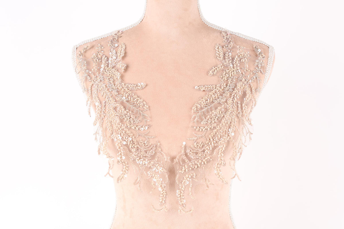 A mannequin wearing a beige dress with intricate lace and sequin details on the shoulders and back.