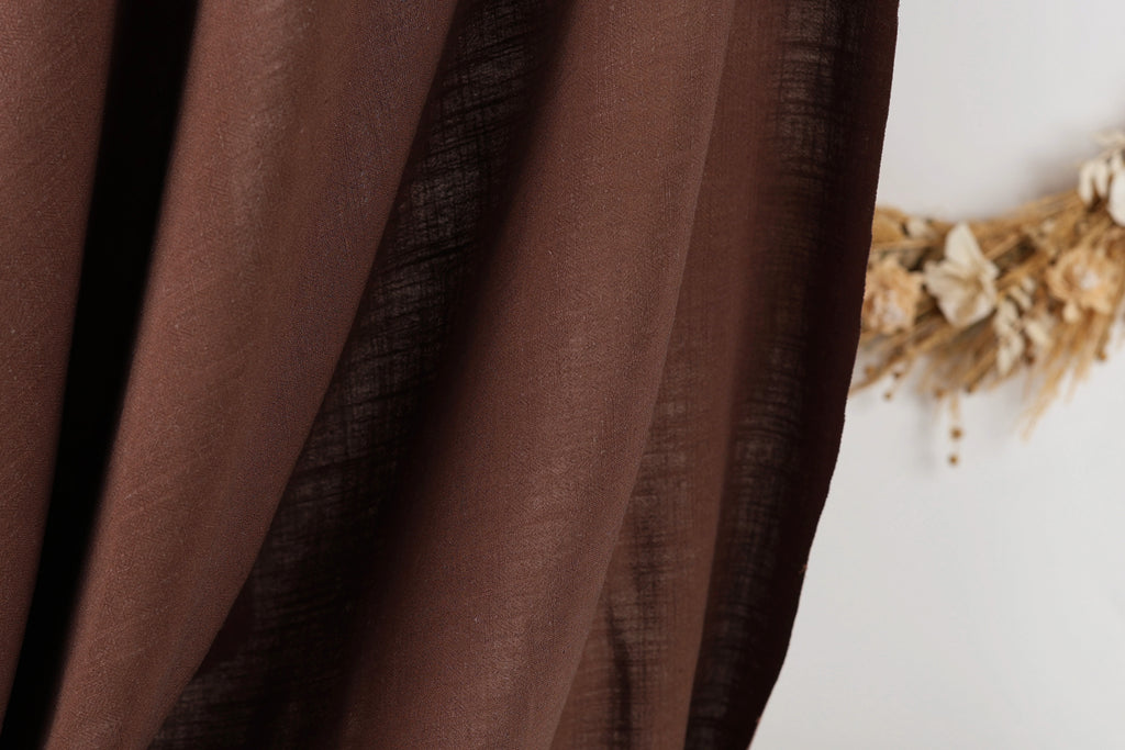 a close-up view of a brown fabric, possibly a curtain or textile, with a blurred background that appears to be a wreath made of dried flowers.