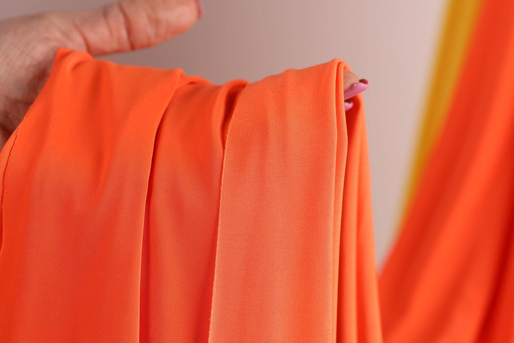 A hand holding a bright orange fabric, with the fabric partially rolled up and held in a hand.