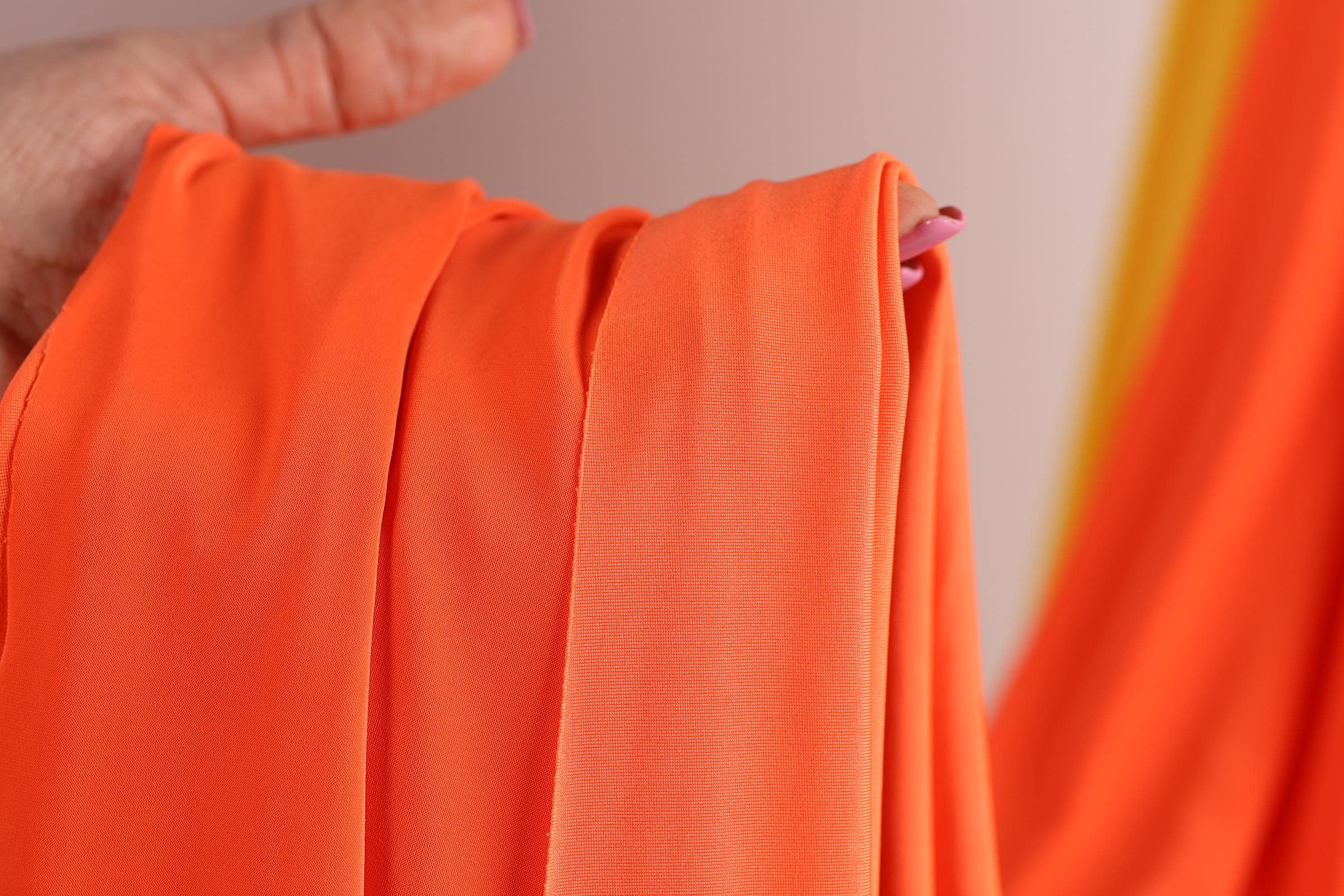 A hand holding a bright orange fabric, with the fabric partially rolled up and held in a hand.