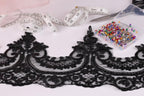 a close-up view of a black lace trim with intricate floral patterns, along with a spool of thread, a pair of scissors, and a container of colorful pins.