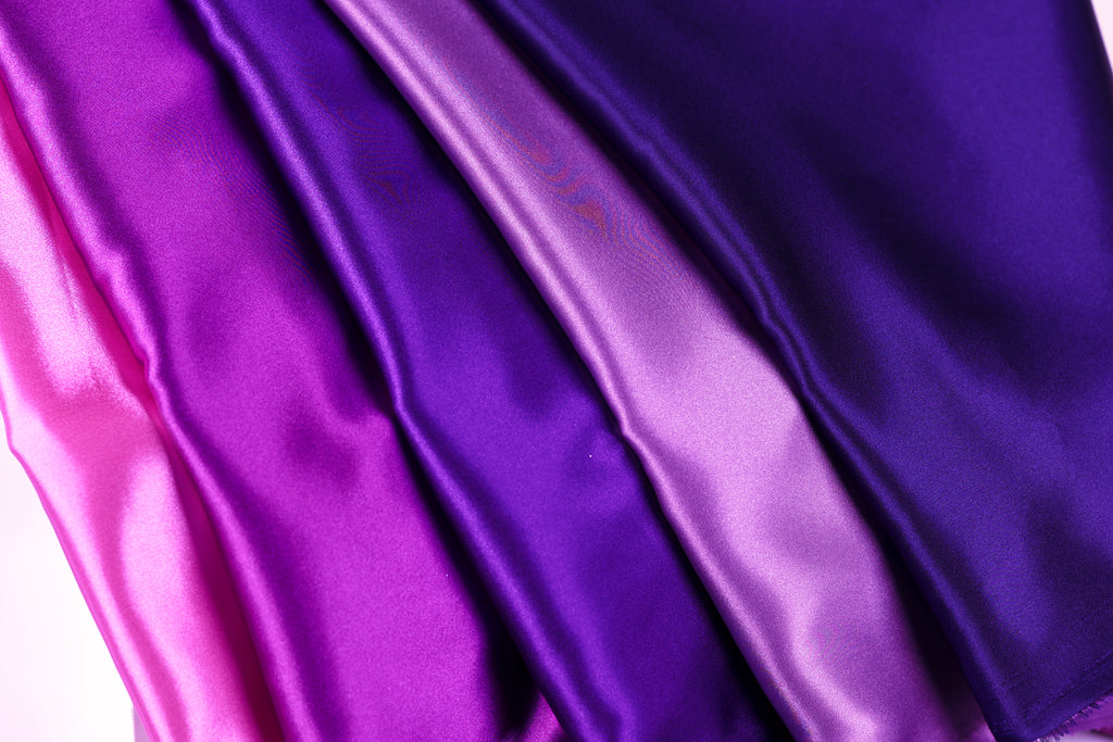 a close-up view of four different colored satin fabrics, with the colors being purple, pink, and blue.