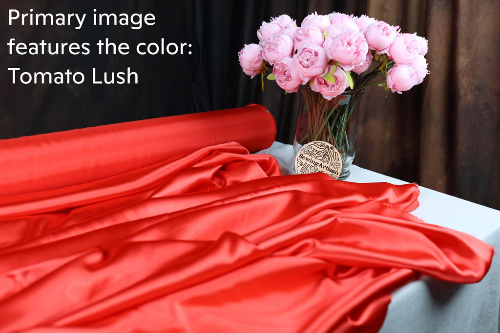 a bouquet of pink flowers in a glass vase, placed on a table with a red satin fabric draped over it.