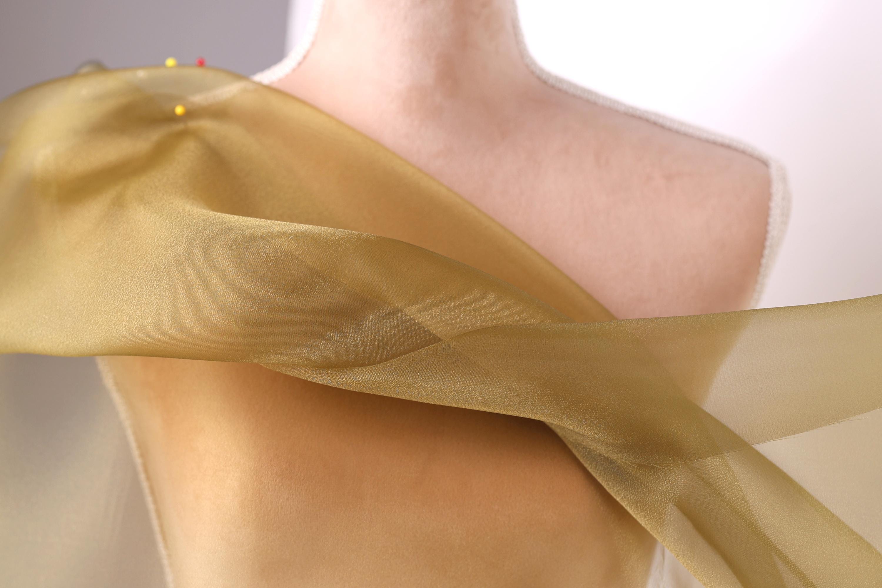 A close-up view of a mannequin wearing a gold-colored fabric draped over its body.