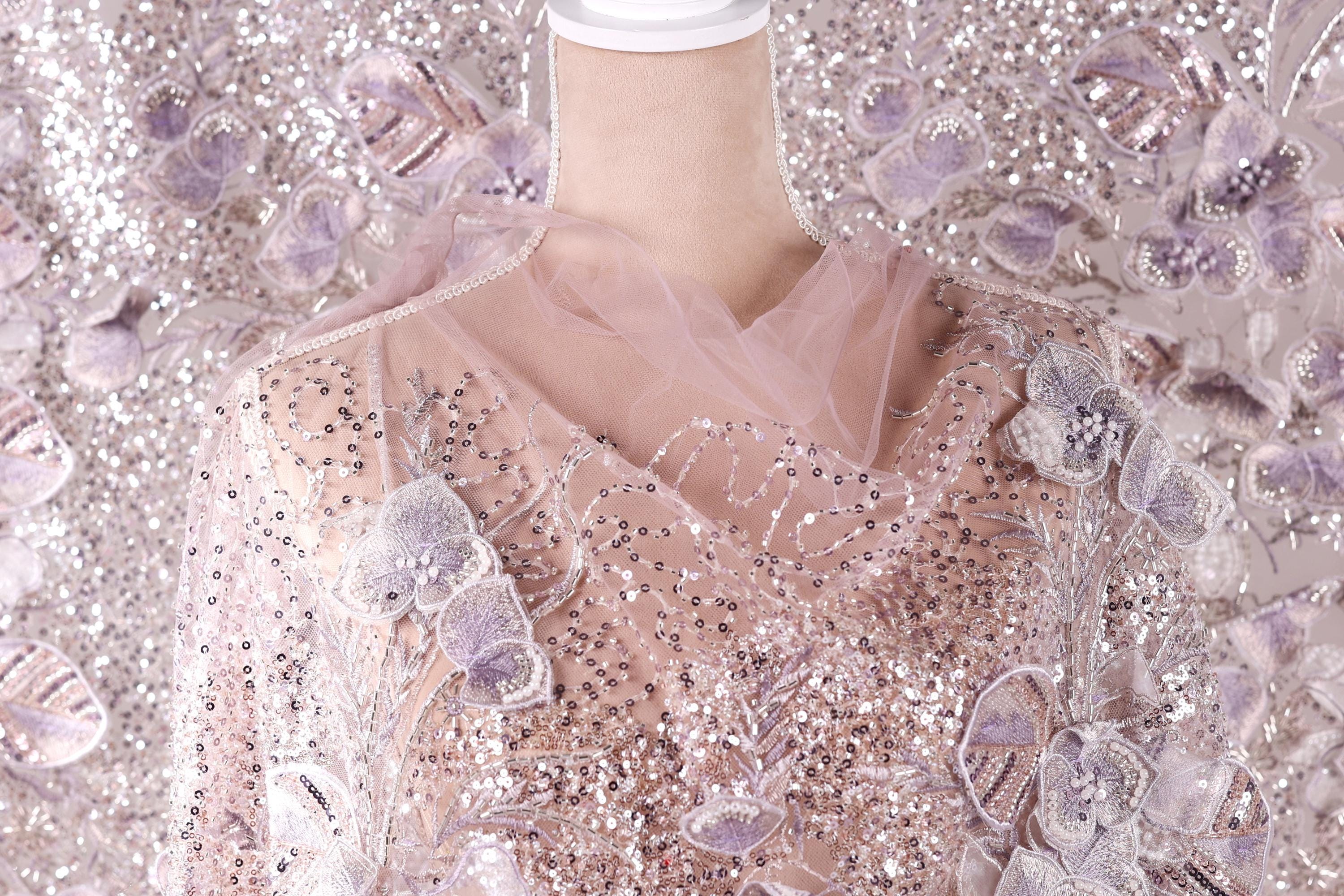 a mannequin wearing a pink and white sequined dress with a sheer, tulle-like fabric draped over it.