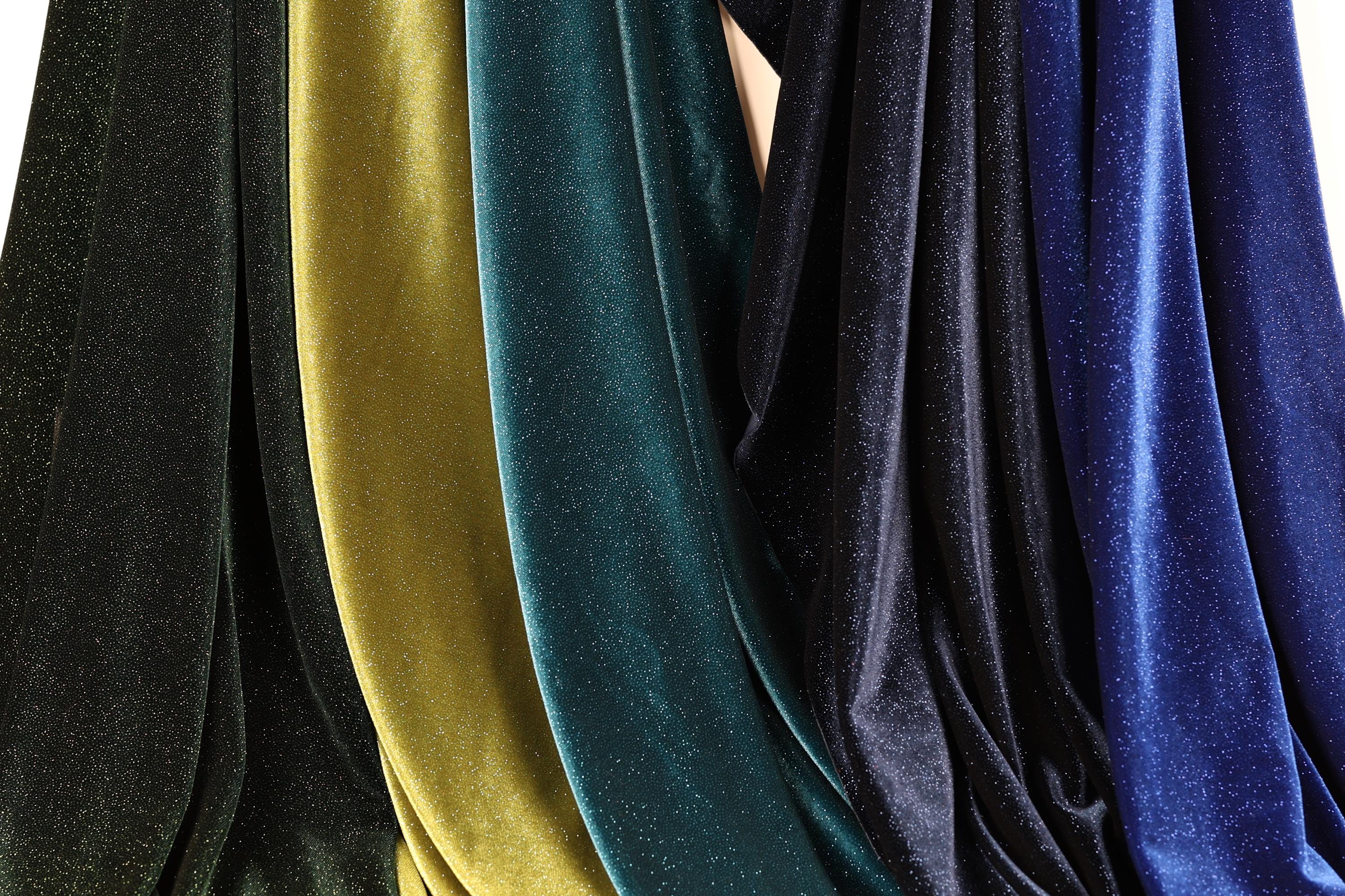 a collection of colorful velvet fabric, with various shades of green, blue, and black. The fabric appears to be made of a shiny, glittery material, giving it a vibrant and eye-catching appearance.