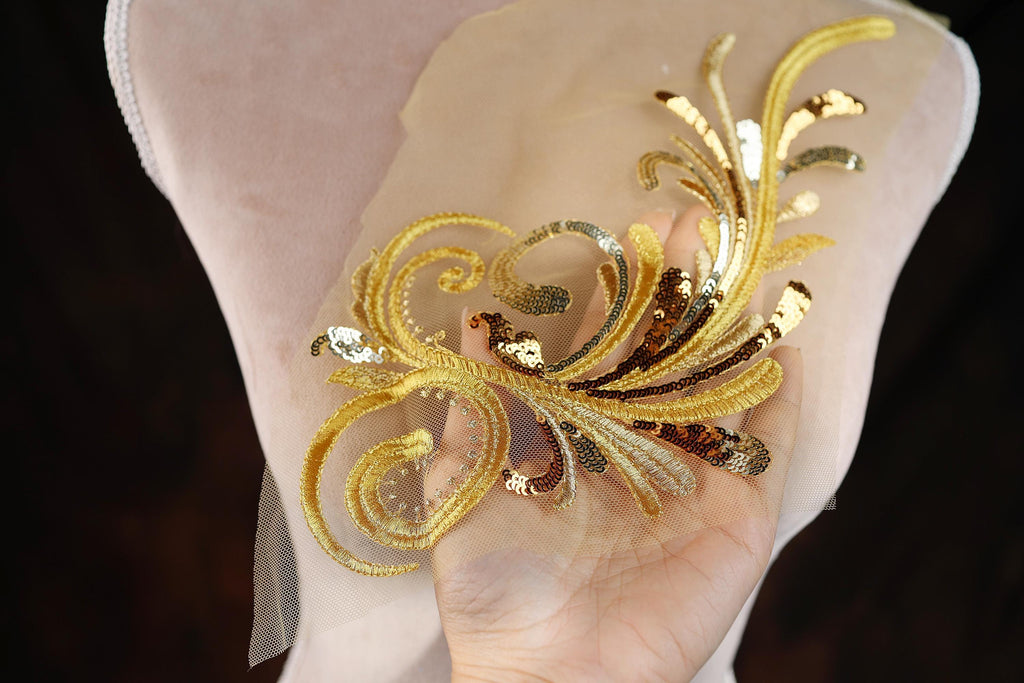 A hand holding a decorative piece of fabric with gold and silver sequin elements.