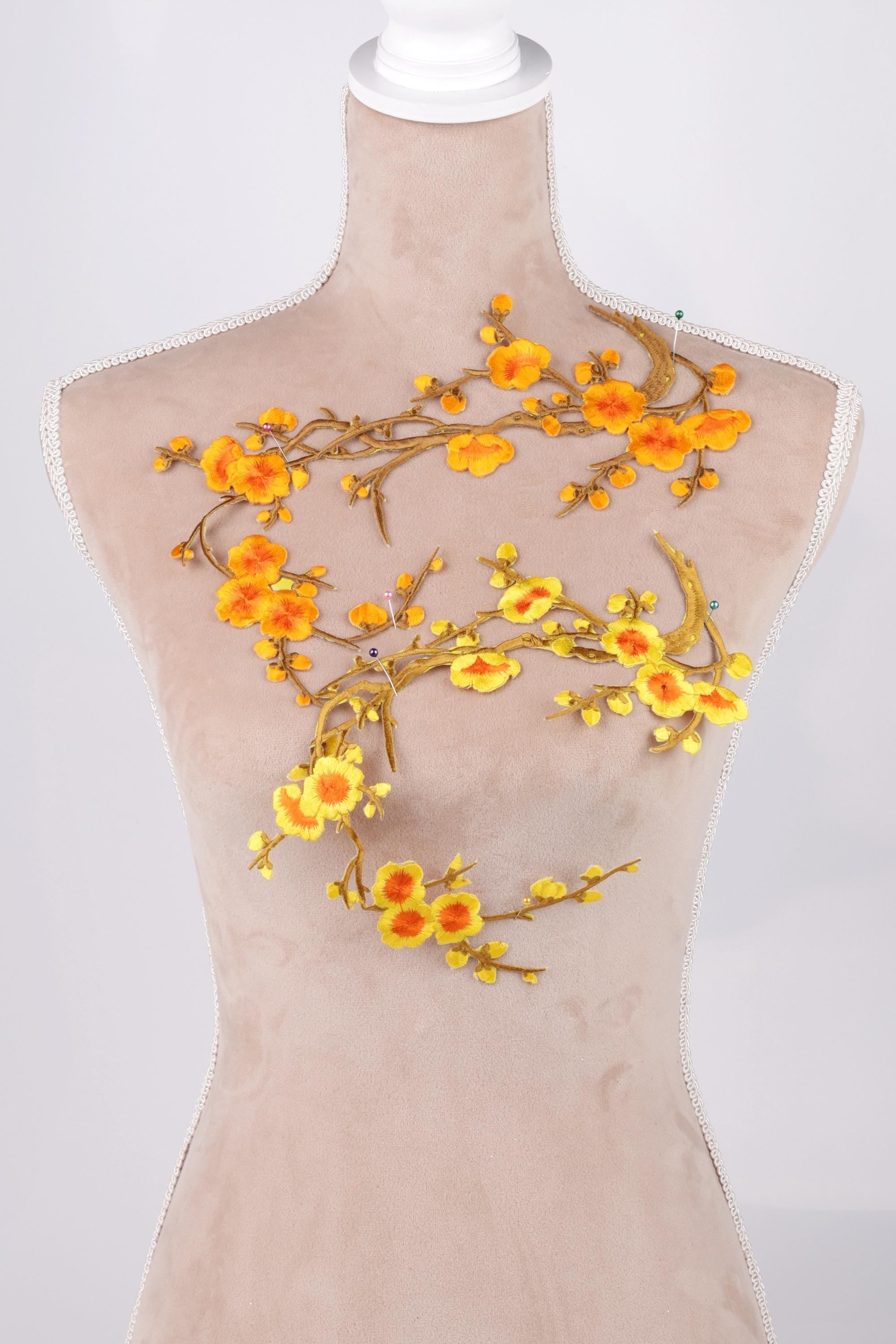 A mannequin wearing a beige dress with a floral embroidered design on the chest area.