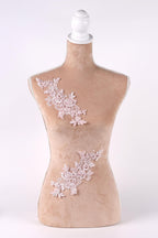 A mannequin with a beige body and a white headpiece, adorned with delicate pink floral embroidery on the bust and waist areas.