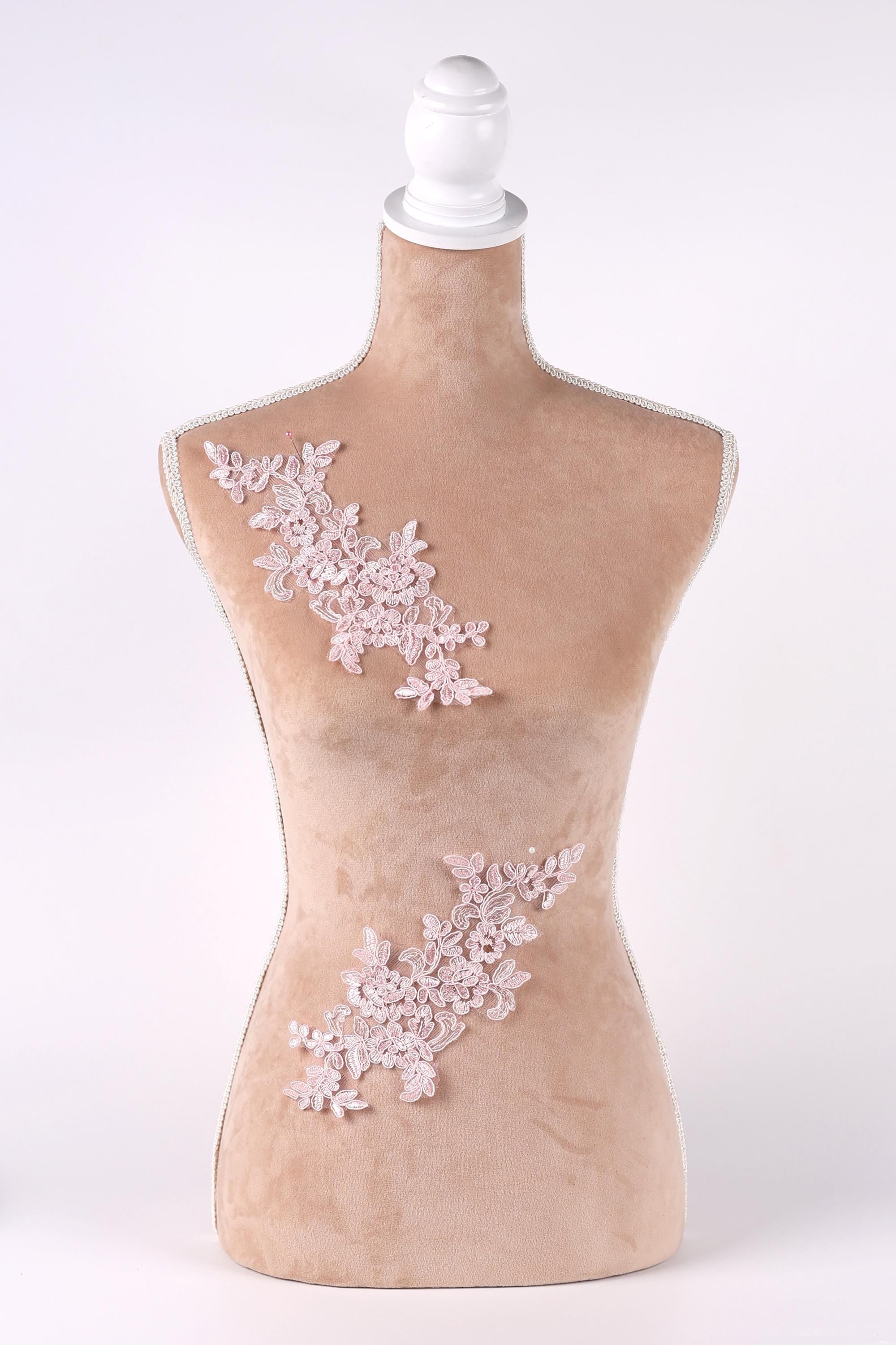 A mannequin with a beige body and a white headpiece, adorned with delicate pink floral embroidery on the bust and waist areas.