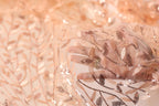 A close-up view of a hand holding a delicate, peach-colored fabric with a leaf-like pattern and sequin accents.