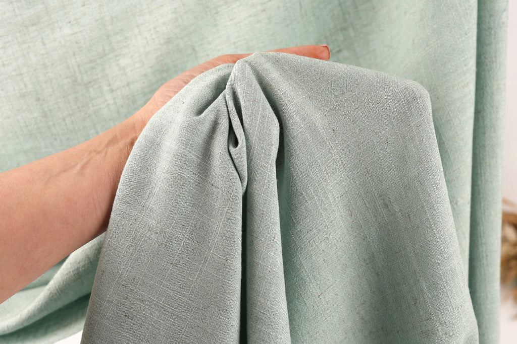 A hand is holding a piece of light green fabric, which appears to be a textile or fabric material.