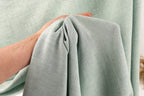 A hand is holding a piece of light green fabric, which appears to be a textile or fabric material.