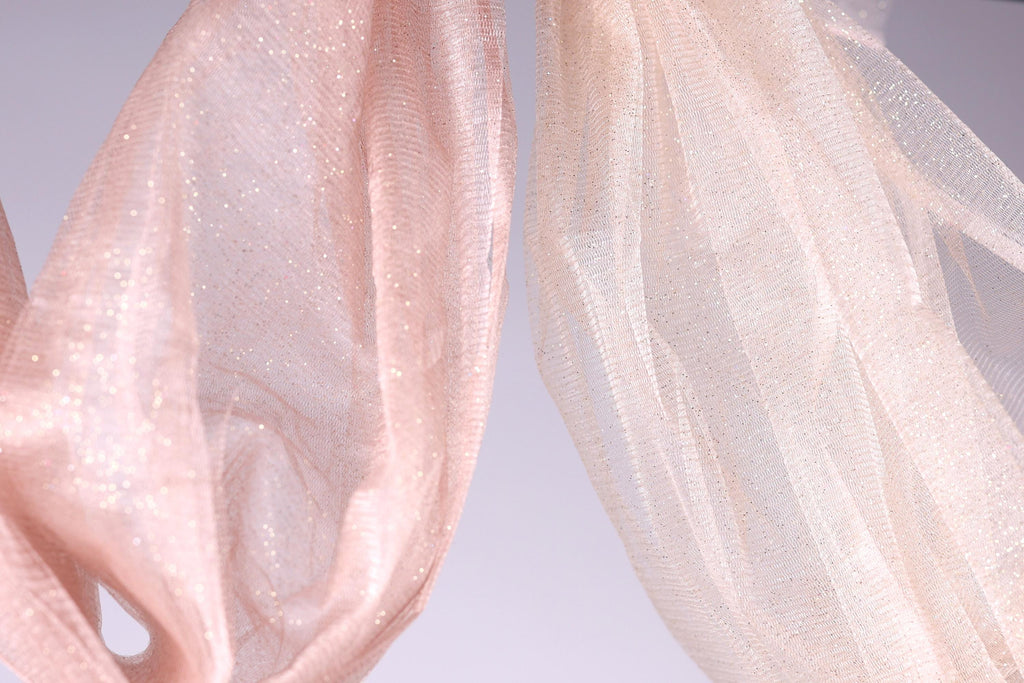 two pieces of fabric, one pink and one white, hanging side by side against a light background.