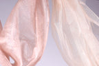 two pieces of fabric, one pink and one white, hanging side by side against a light background.