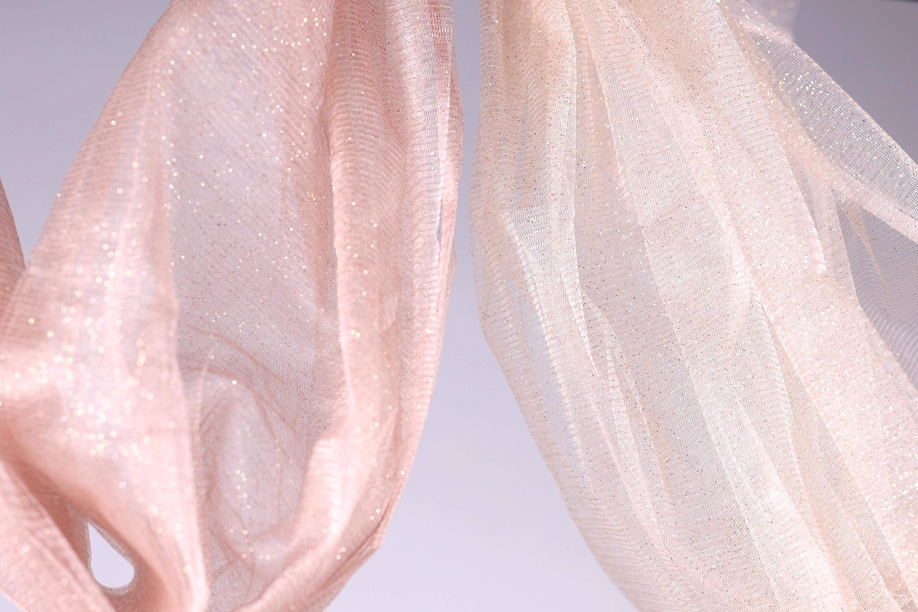 two pieces of fabric, one pink and one white, hanging side by side against a light background.