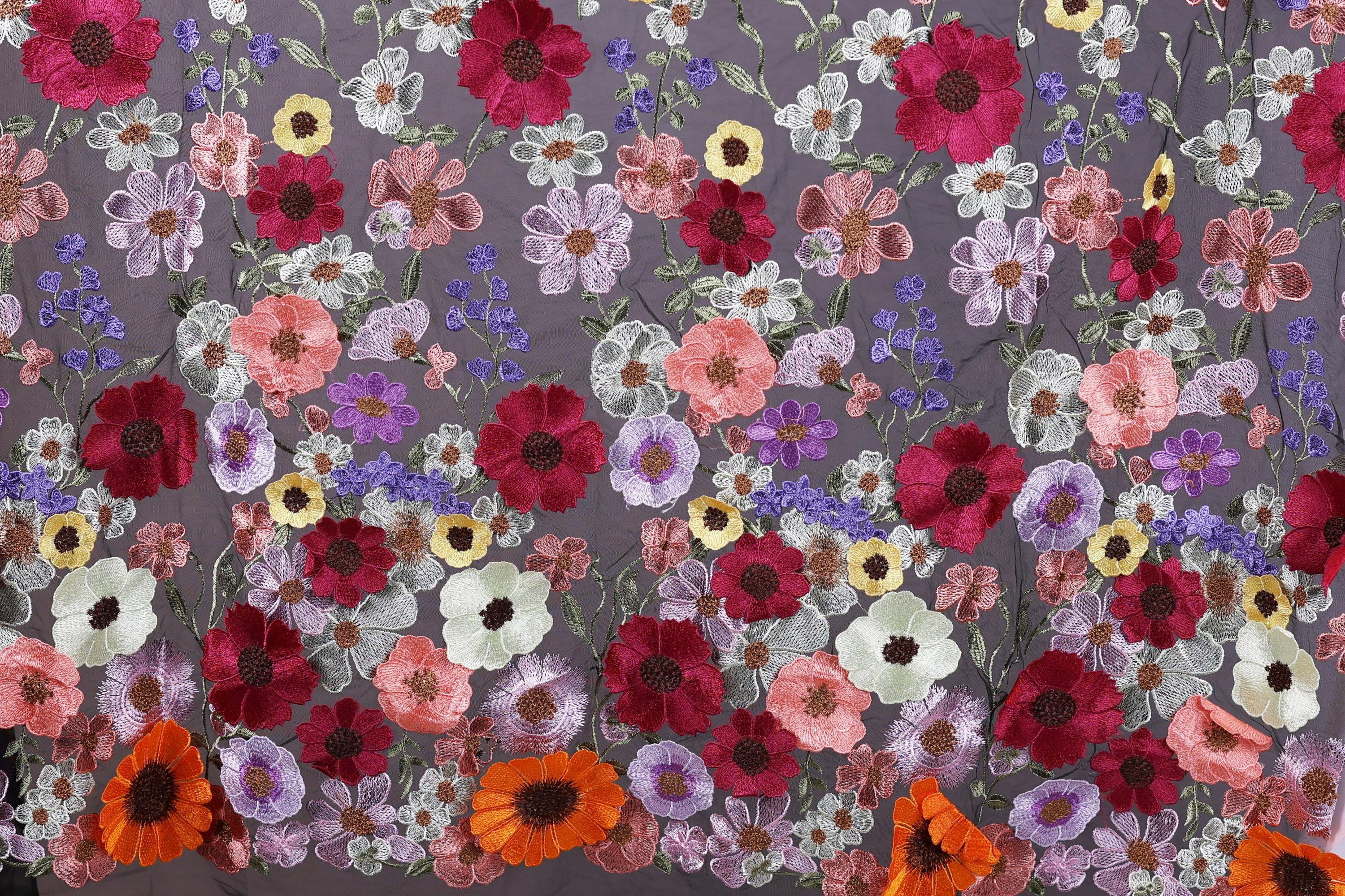 a vibrant and colorful floral pattern, with a variety of flowers in shades of red, pink, white, and purple. The flowers are intricately embroidered or sewn onto a fabric, creating a visually striking and detailed design.