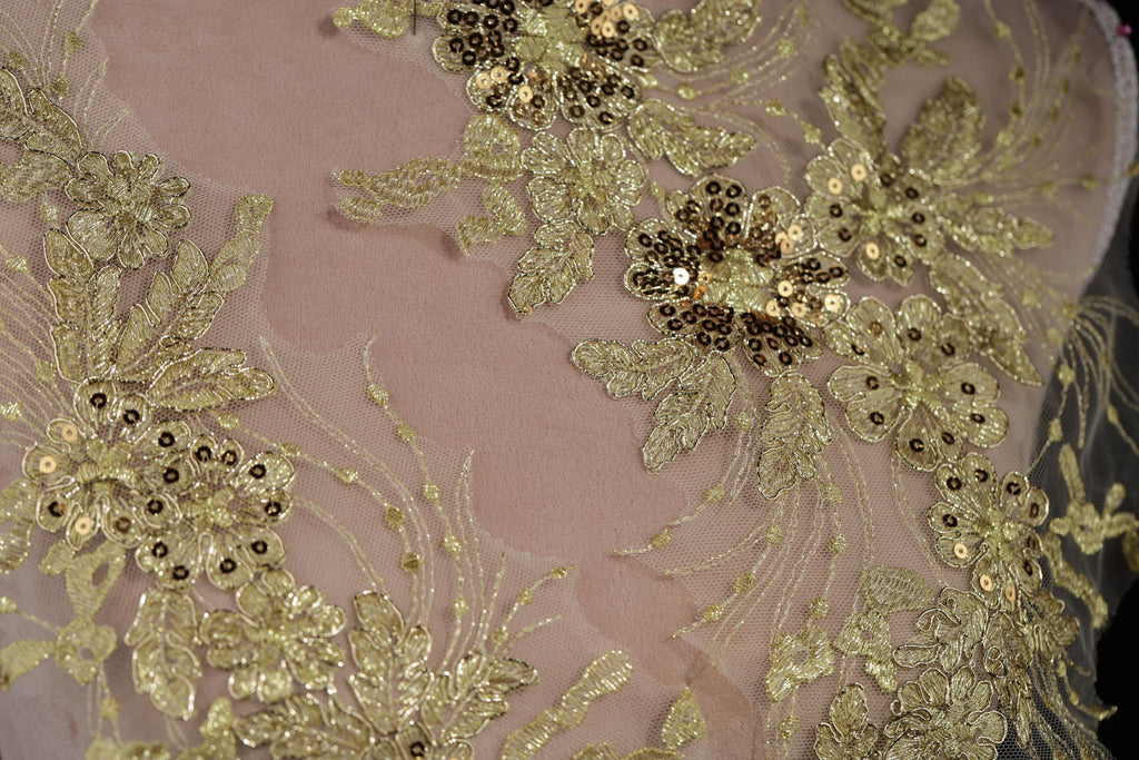 a close-up view of a delicate, intricate piece of fabric adorned with gold and white embroidered flowers and leaves.