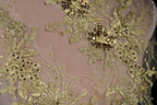 a close-up view of a delicate, intricate piece of fabric adorned with gold and white embroidered flowers and leaves.