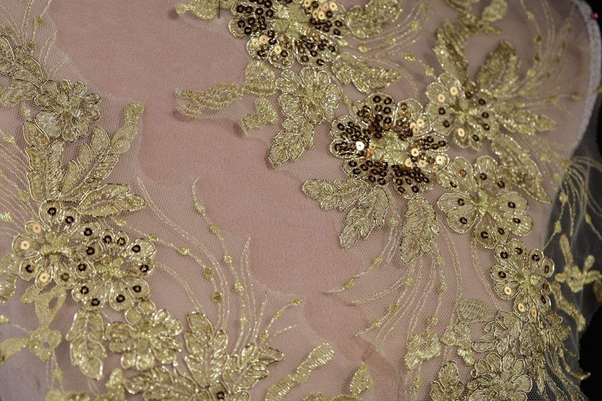 a close-up view of a delicate, intricate piece of fabric adorned with gold and white embroidered flowers and leaves.