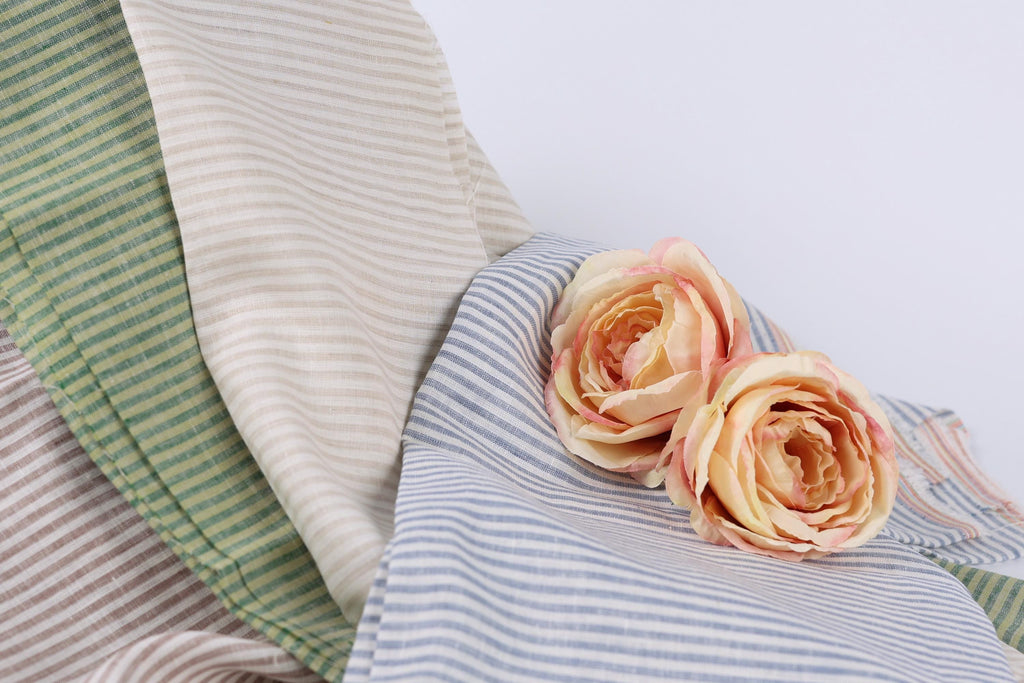 two pink roses resting on a striped fabric, which appears to be a mix of green, white, and blue stripes.