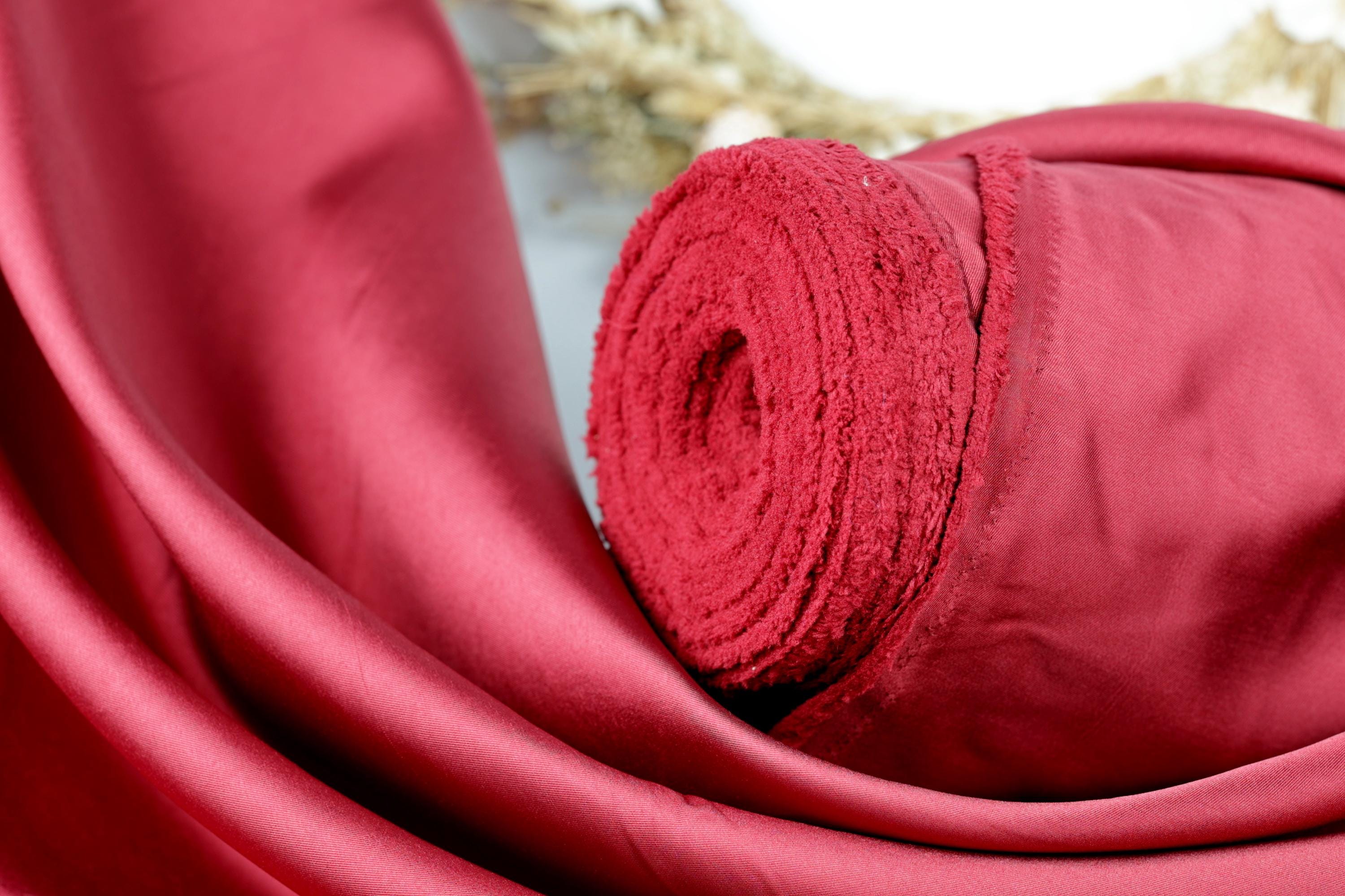 A close-up view of a red satin fabric, with a rolled-up piece of the fabric visible in the foreground.