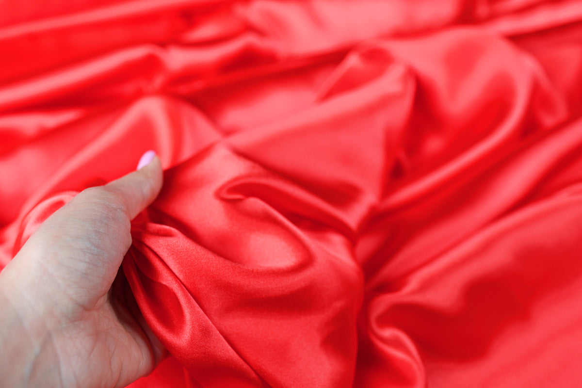 A hand is holding a piece of red satin fabric, with the fabric's folds and creases visible.