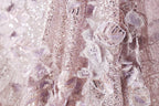 The image is a close-up of a delicate, intricately designed fabric with a pink and white color scheme. The fabric features a variety of textures, including sequins, lace, and floral elements, creating a visually appealing and detailed appearance.