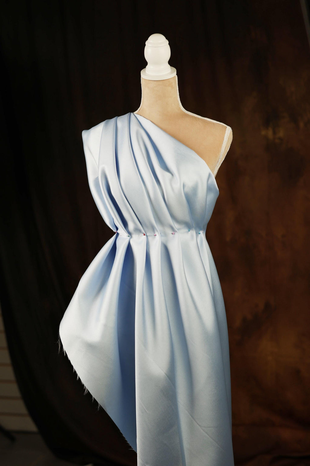 A mannequin wearing a light blue one-shoulder dress with a draped, flowing design.